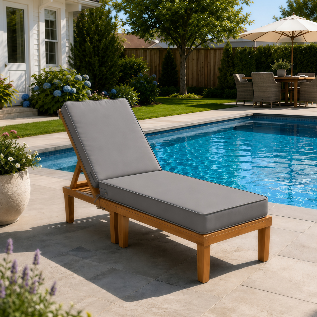 Teak wood outdoor lounge chair with a thick, grey water-resistant cushion beside a backyard swimming pool.