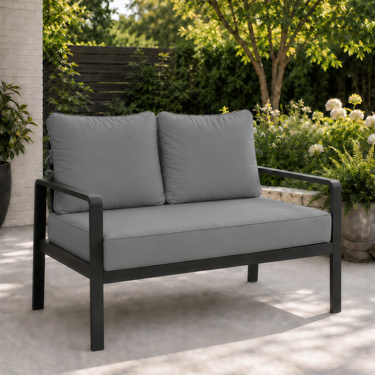 Sage light gray outdoor loveseat cushions on a modern black metal frame set on a patio.