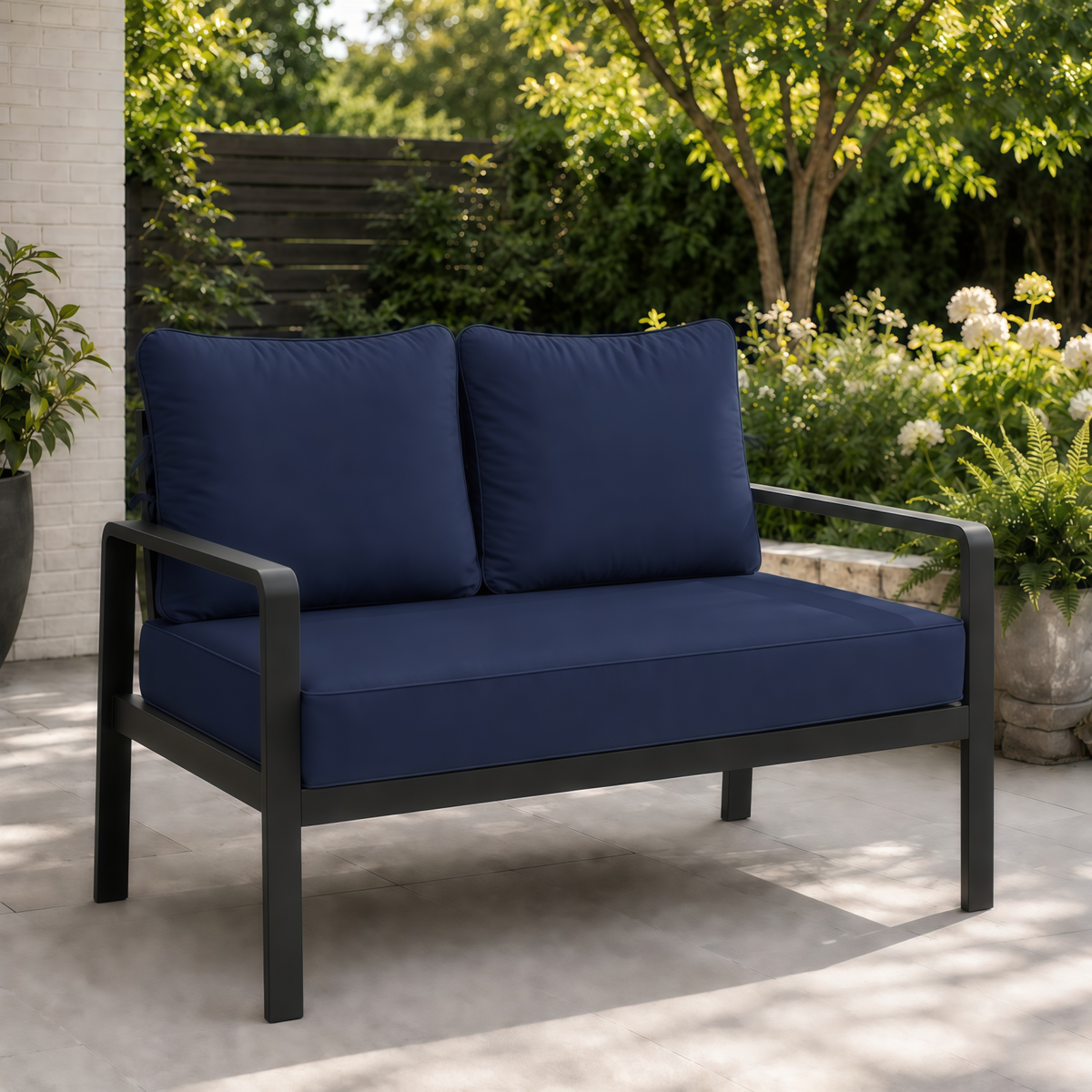Sage blue outdoor loveseat cushions on a modern black metal frame set on a patio.